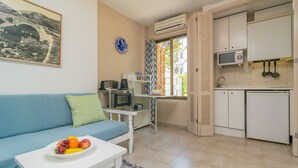 A compact living space with a sofa, a dining table with fruit, a kitchenette with a microwave, and a window with curtains. - ENCINAS 1 - Apartment with terrace in Port De Pollença. Free WiFi (Pollença)