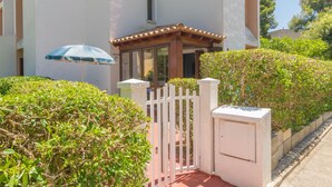 A gated entrance with a wooden gate and a white wall, surrounded by lush greenery. - ENCINAS 1 - Apartment with terrace in Port De Pollença. Free WiFi (Pollença)