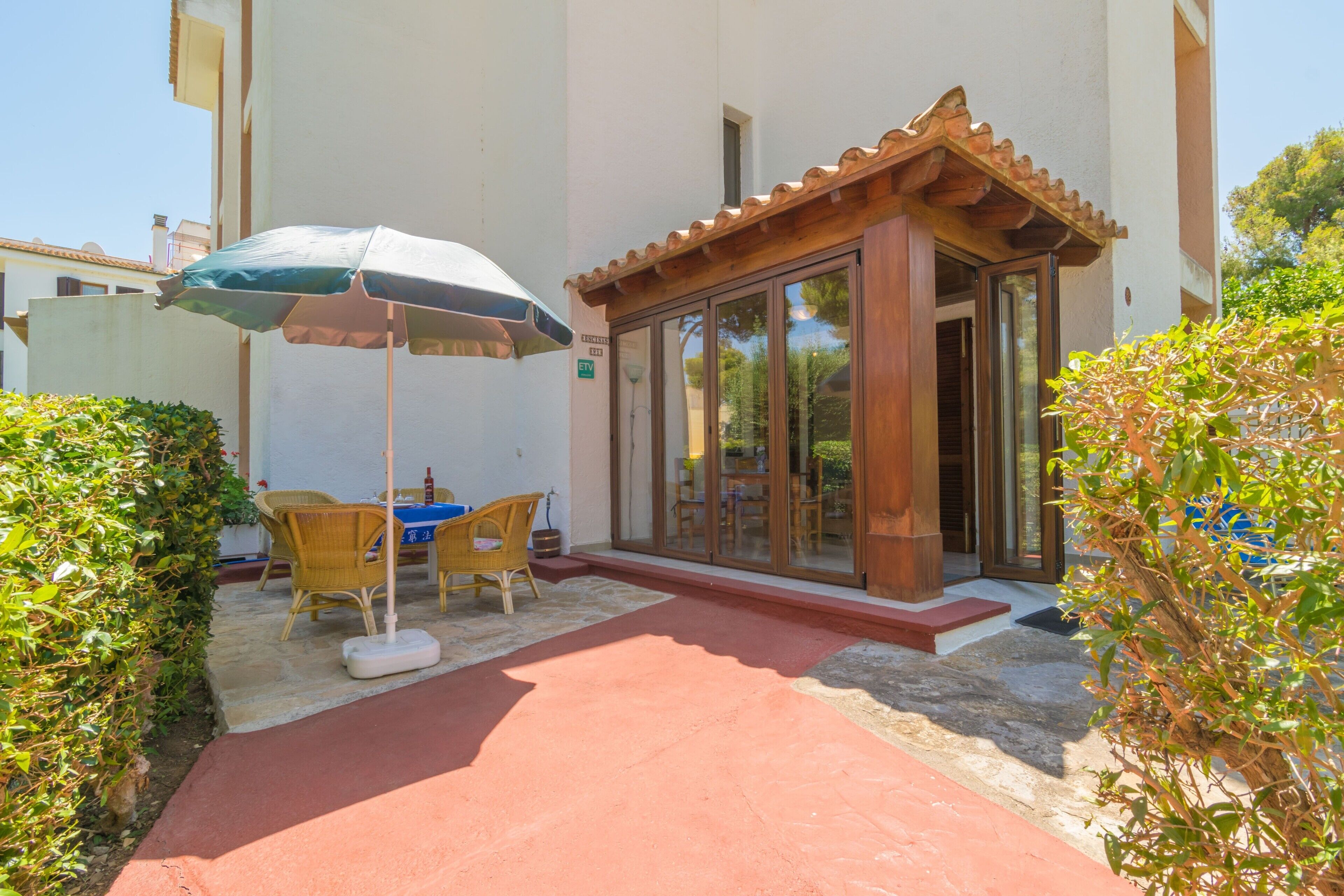A covered outdoor seating area with a table and chairs, a wooden pergola, and a glass door entrance to a building.