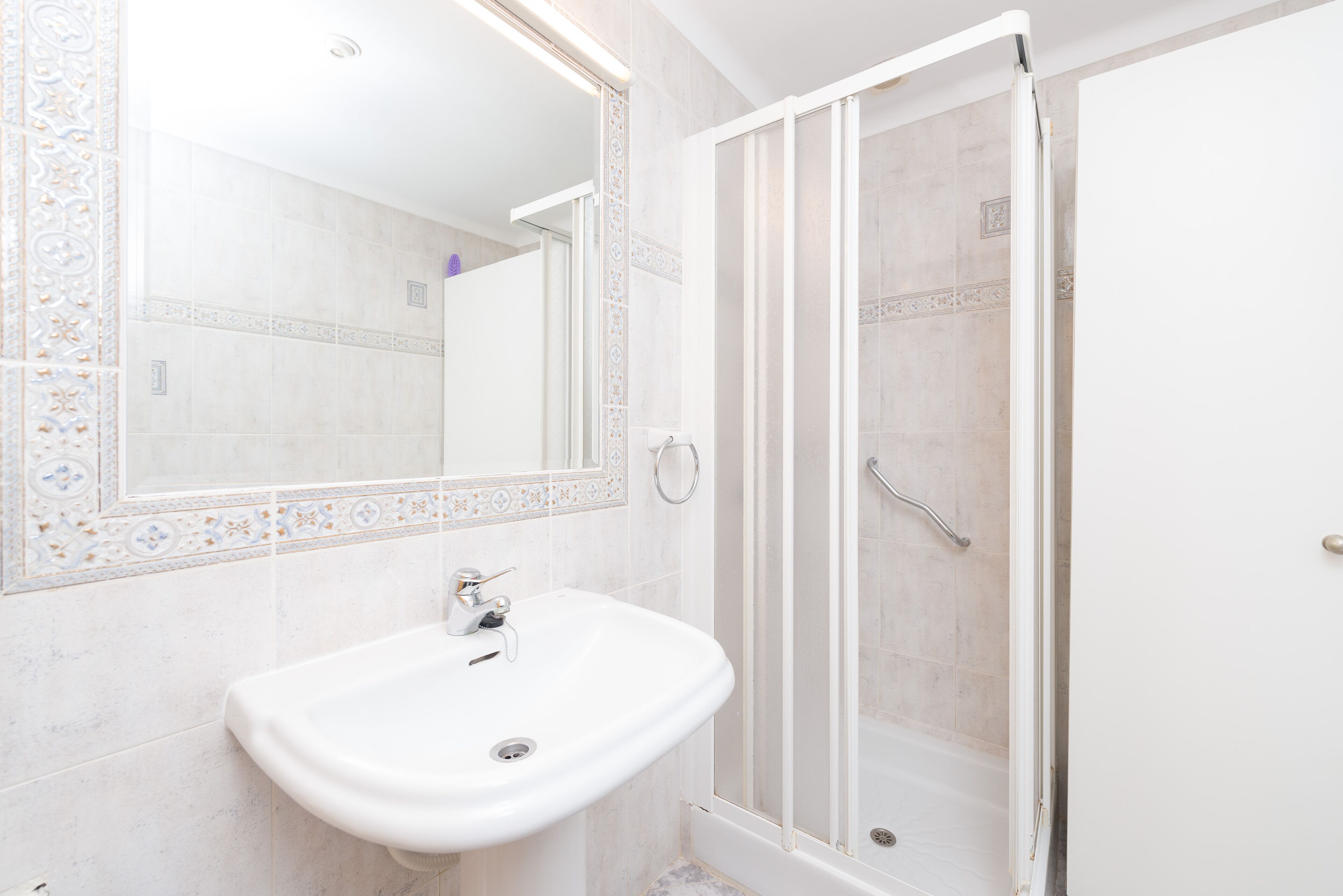 A bathroom with a white sink, a mirror, and a glass-enclosed shower.