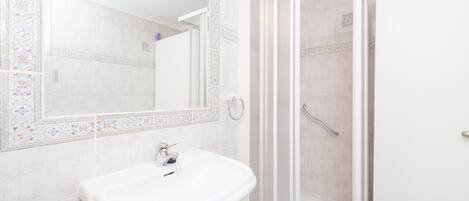 A bathroom with a white sink, a mirror, and a glass-enclosed shower.