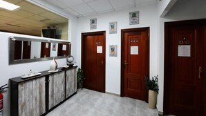 A reception area with a wooden reception desk, a mirror, and a fire extinguisher. There are two wooden doors with signs above them. - Albergue Arraigos - Hostel (Melide)