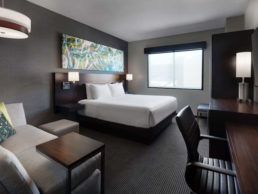 A hotel room with a bed, a sofa, a desk, and a large window.