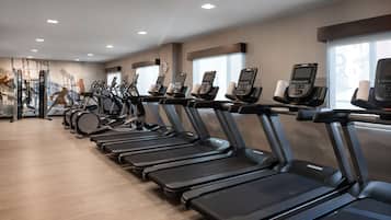 Un gimnasio con varias cintas de correr alineadas, una máquina de pesas y una pared con un mural.