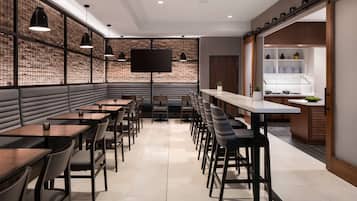 Un ristorante moderno con un lungo bancone, cabine e una zona cucina visibile attraverso una porta aperta.