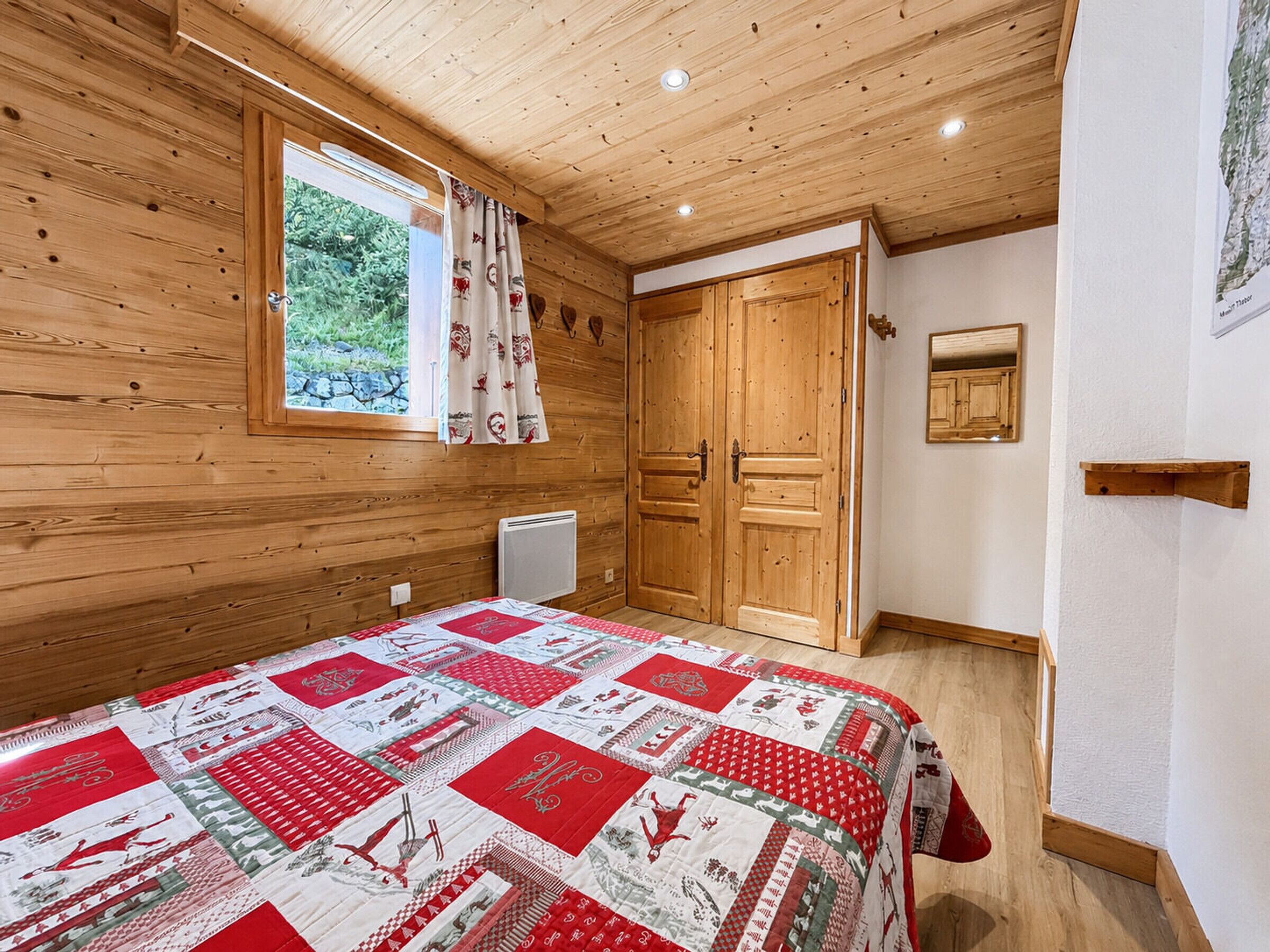 A wooden-paneled room with a bed, a window with curtains, a radiator, and a door.