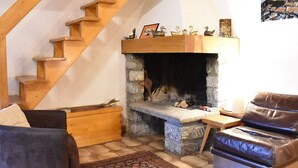Un salon chaleureux avec une cheminée en pierre, un escalier en bois et un canapé en cuir.