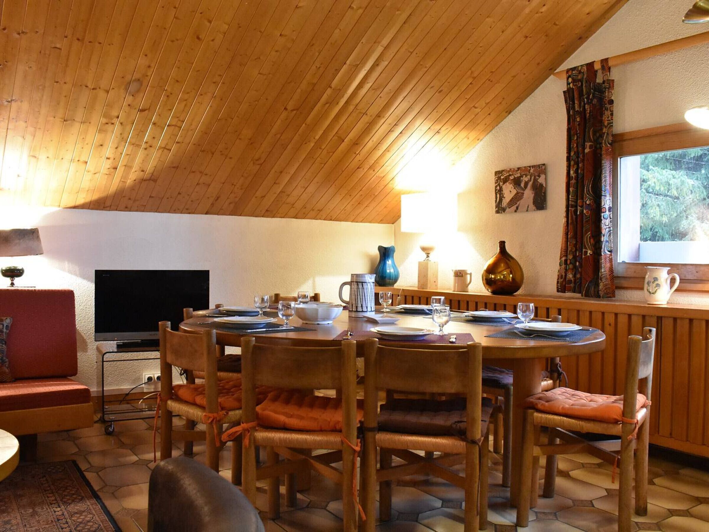 Un coin repas accueillant avec un plafond en bois, un téléviseur et une fenêtre avec des rideaux.