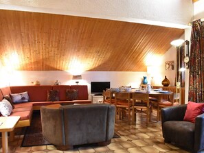 Ett mysigt vardagsrum med ett träpanelat tak, en soffa, ett soffbord och en matplats med stolar och ett bord.