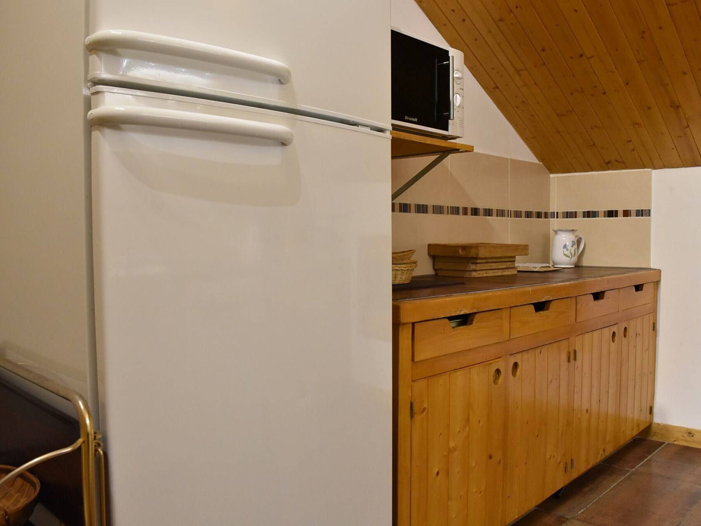 A kitchen with a white refrigerator, wooden cabinets, a microwave on a shelf, and a tiled backsplash.