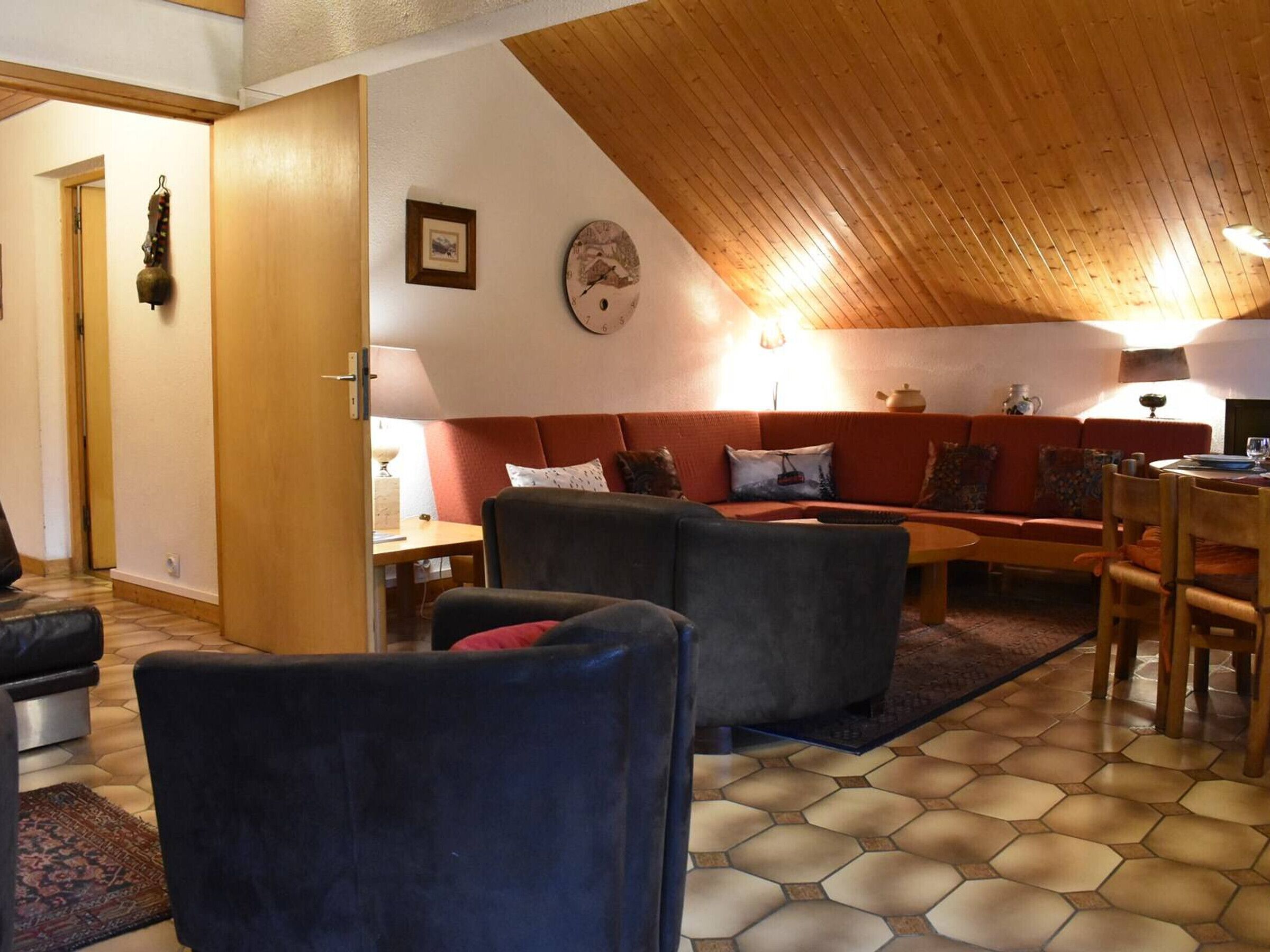 A cozy living room with a wooden ceiling, a sofa set, a dining table, and a clock on the wall.