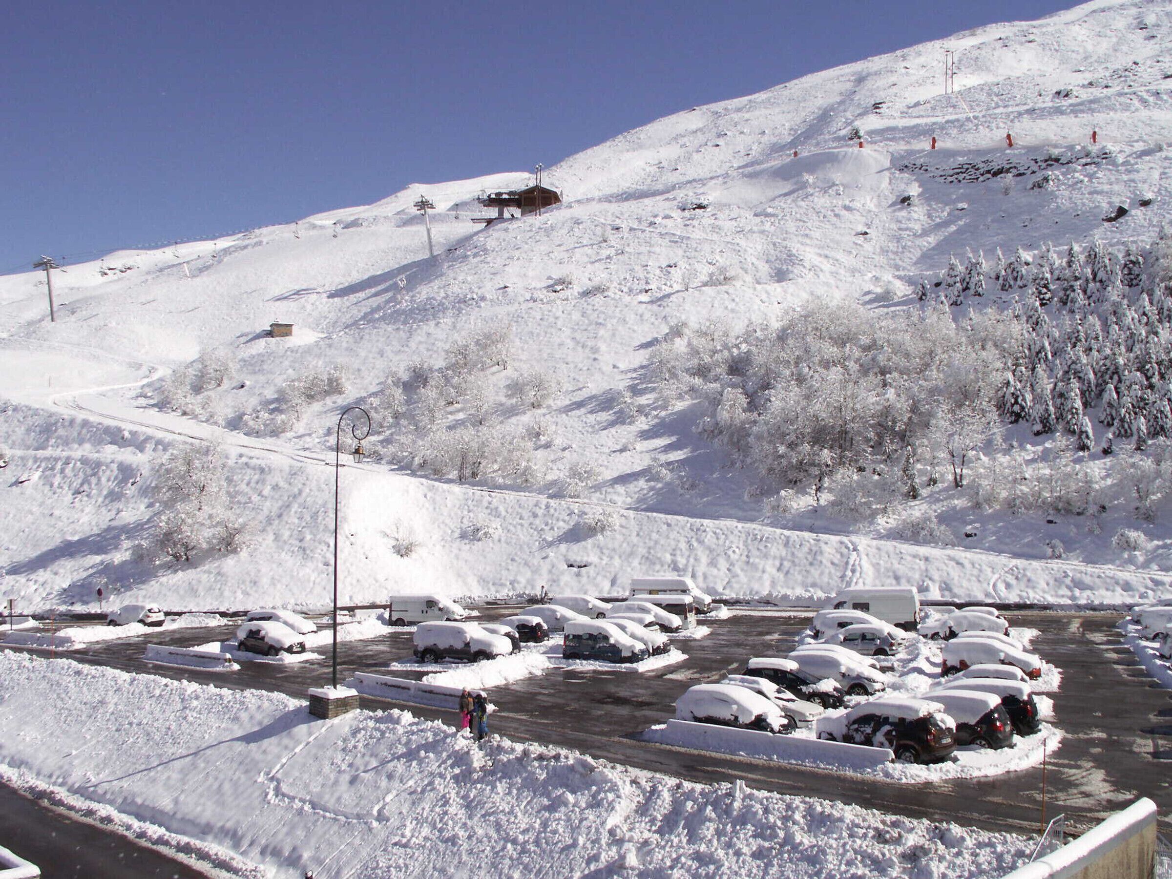 Un estacionamiento cubierto de nieve con coches y un telesilla en una montaña nevada.