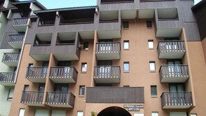 A multi-story apartment building with balconies, a central entrance, and a sign indicating 'Astral Estate'. - Economical studio for 3 in the heart of Les Menuires (Les Menuires)