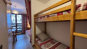 A bunk bed room with a wooden ladder, a small table, and a chair. - Economical studio for 3 in the heart of Les Menuires (Les Menuires)