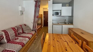 A compact room with a wooden dining table, a sofa, a kitchenette with a microwave, and a small refrigerator. - Economical studio for 3 in the heart of Les Menuires (Les Menuires)