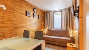 A room with a wooden wall, a sofa, a table with chairs, a clock, and a window with curtains. - Renovated studio 4 pers, balcony, center Plagne Bellecôte (Plagne Bellecôte)