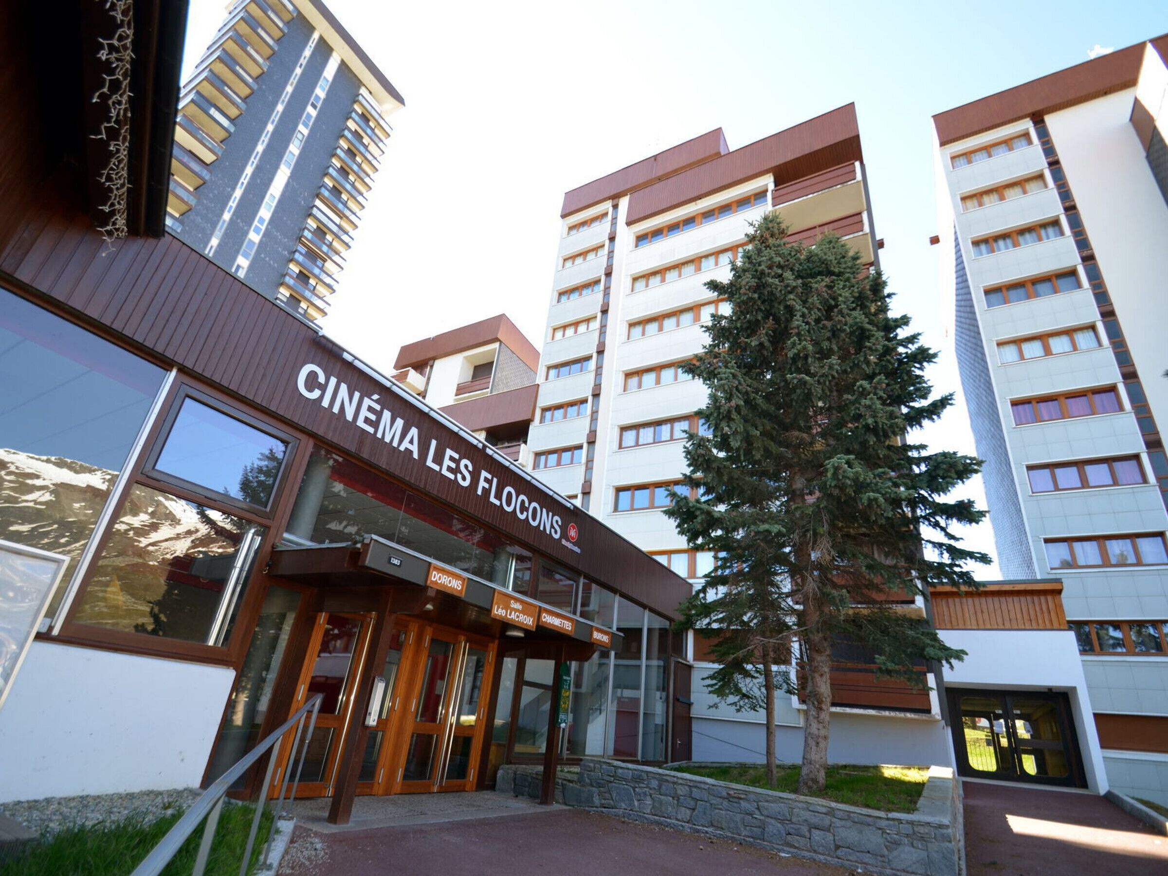 A modern building with a cinema entrance, multiple floors, and a prominent tree in front.