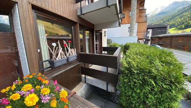 Ein Holzhaus mit Balkon, Bank und Blumenbeet mit Studentenblumen.