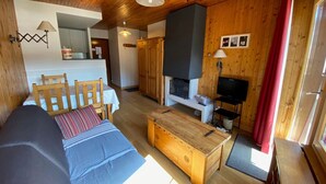 Ein gemütliches Blockhaus-Interieur mit Holzbalkendecke, einer Couch, einem Esstisch, einem Kamin und einem Fernseher.