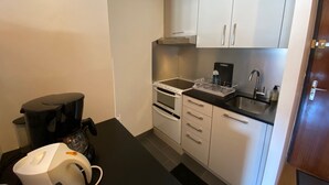 Eine kleine Küche mit weißen Schränken, einer schwarzen Arbeitsplatte, einem eingebauten Backofen, einem Spülbecken und einer Kaffeemaschine.