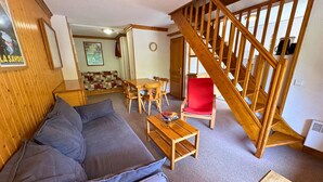 A cozy living room with a wooden staircase, a sofa, a dining table, and a red chair.