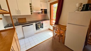 A compact kitchen with white cabinets, a built-in oven, a coffee maker, and a dining area with a chair.