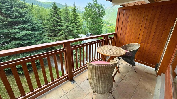 A balcony with a wooden railing, two wicker chairs, and a view of a mountainous landscape.