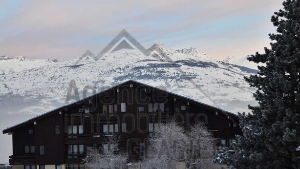 Un edificio grande con múltiples ventanas y techo inclinado, rodeado de nieve y árboles.