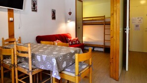 Una habitación con una mesa de comedor, sillas, un sofá rojo, una cama litera y un televisor.