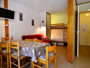 A room with a dining table, chairs, a red sofa, a bunk bed, and a television.