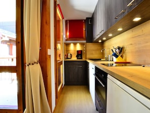 A compact kitchen with wooden cabinets, a red upper cabinet, a coffee maker, and a sink.