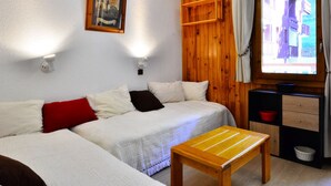 Una habitación con pared de madera, una cama, una mesita, un ventanal con cortinas y un cuadro en la pared.