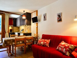 Een compacte leefruimte met een eethoek, kitchenette en een rode bank met decoratieve kussens.