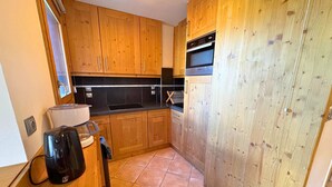 Eine kompakte Küche mit Holzausbau, einem eingebauten Backofen und einer Kaffeemaschine.