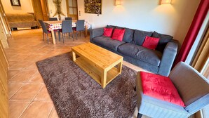 Ein Wohnzimmer mit grauem Sofa, roten Kissen, einem Holztisch und einem Essbereich mit Tisch und Stühlen.