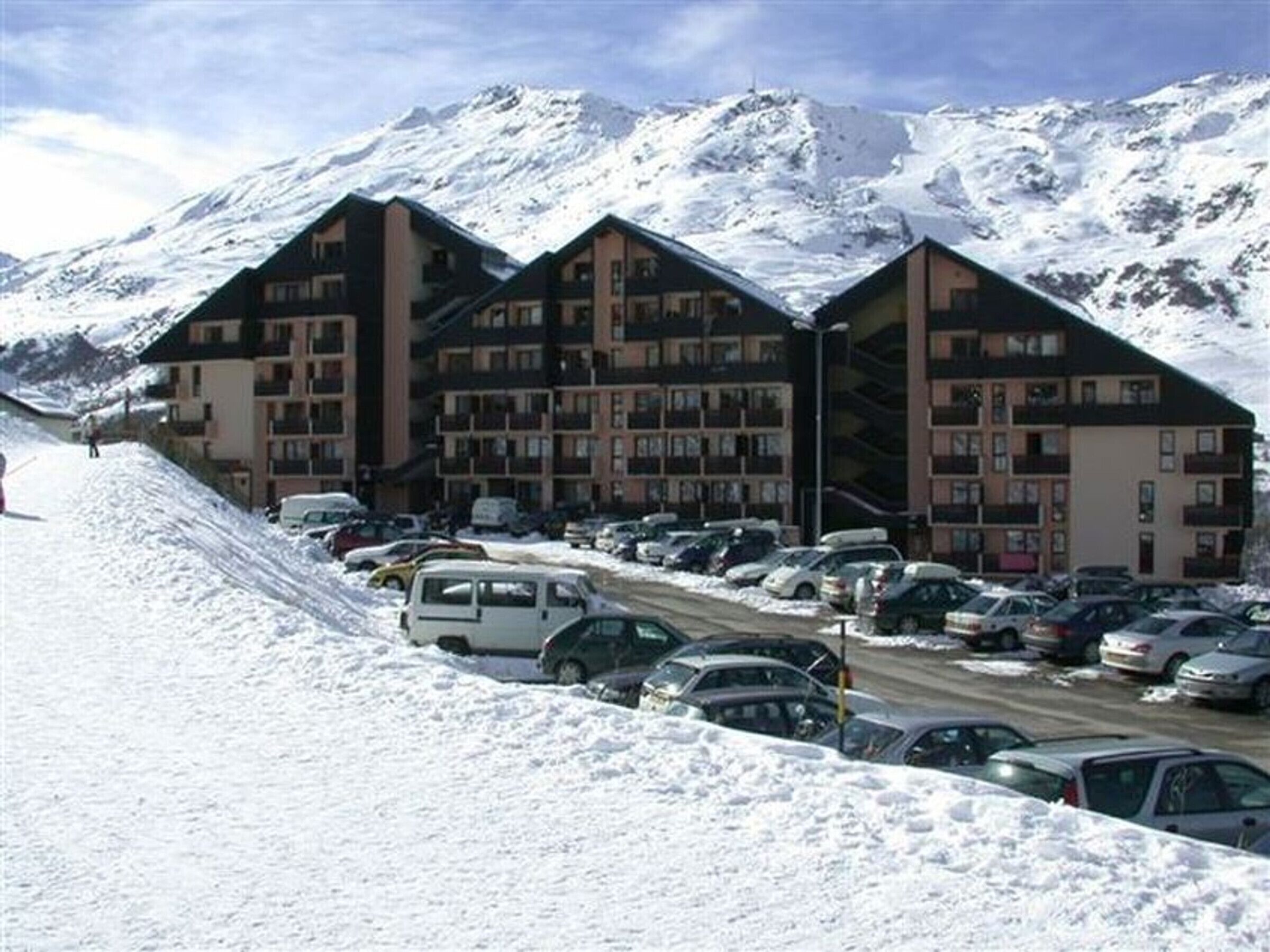 Un hotel con varias construcciones, un estacionamiento con coches y una montaña nevada al fondo.