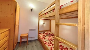 Une chambre avec un lit superposé, une armoire en bois, une petite table et un radiateur fixé au mur.