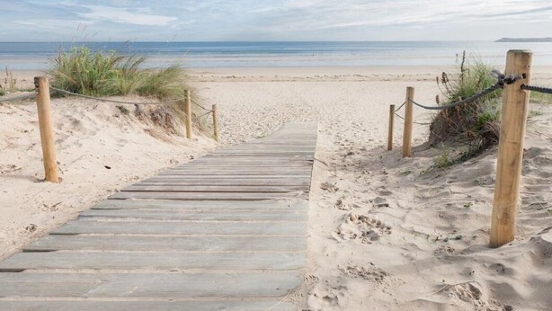 En träpromenad som leder till en sandstrand med fri utsikt över havet.