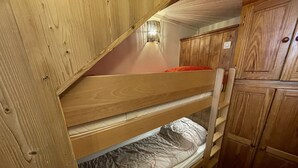 A bunk bed with wooden headboard and footboard, a red pillow, and a white mattress.