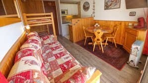 Une pièce chaleureuse avec un lit superposé en bois, une petite table à manger avec des chaises, un coin cuisine et un radiateur.
