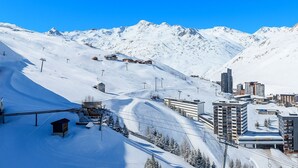 Un paysage de montagne enneigé, avec des pistes de ski, un petit chalet et des bâtiments modernes.
