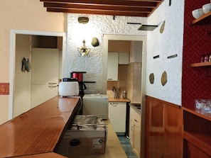 A compact kitchen with a wooden table, a coffee maker, a kettle, and a small refrigerator. - Cauterets: 2 BR Apartment, 8 Guests, Wifi & Parking (Cauterets)