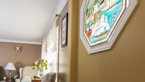 Una habitación con piso de madera, una silla con estampado de la Torre Eiffel, una lámpara y un ventanal de vidrio emplomado montado en la pared.
