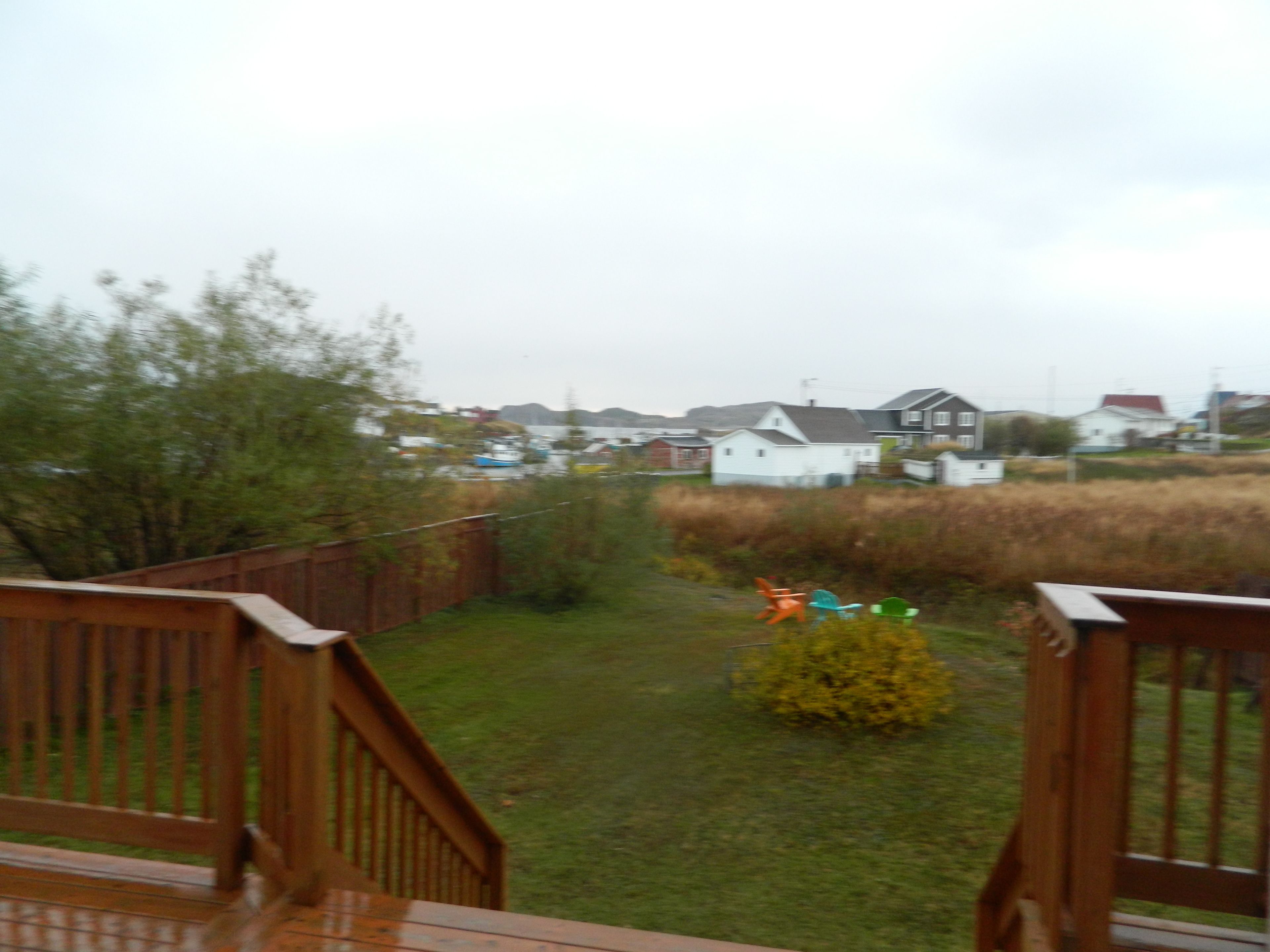 A wooden deck with a view of a grassy yard and houses in the background.