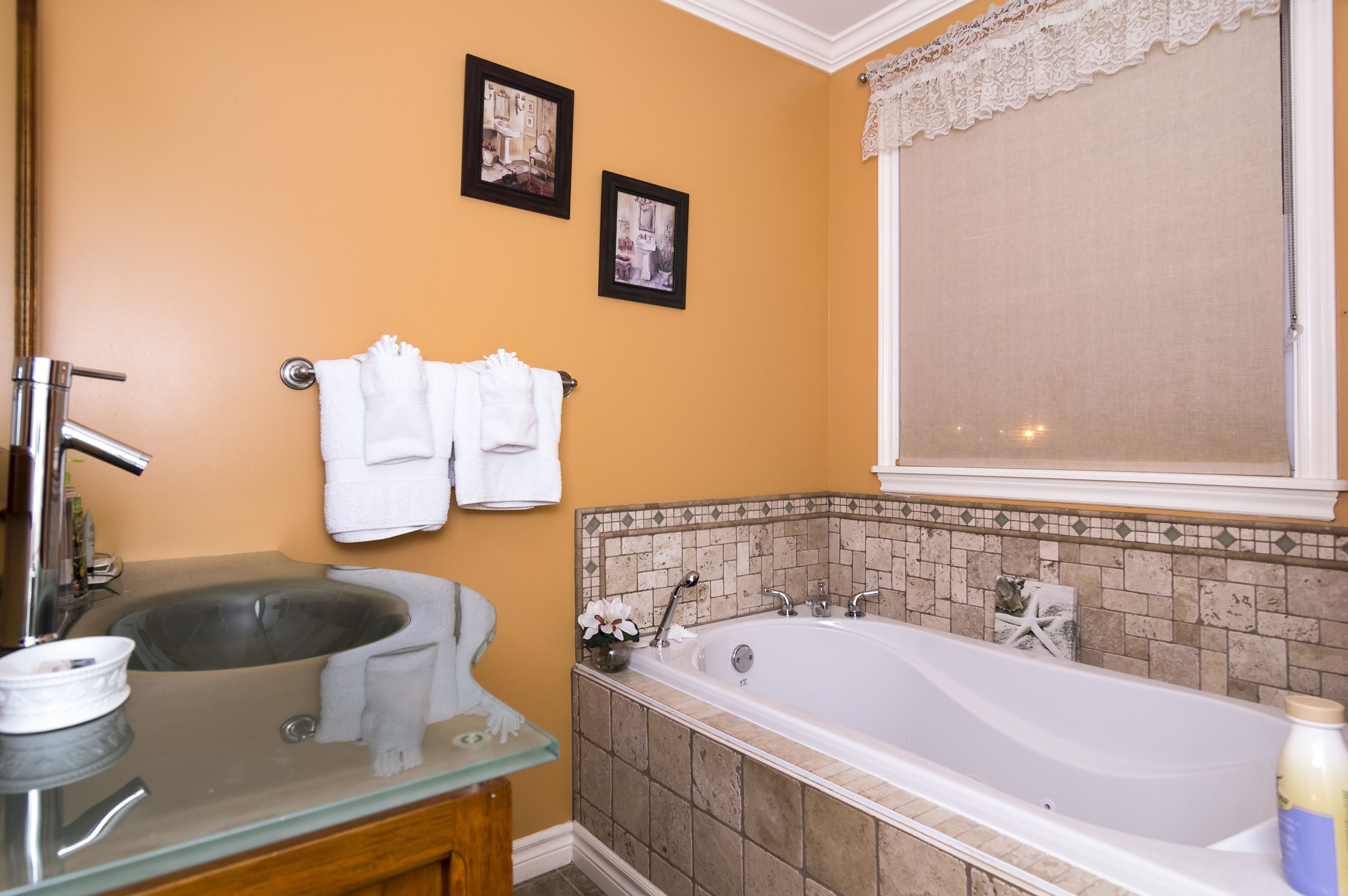 Ein Badezimmer mit einem Glaskonstruktion-Waschbecken, einer Badewanne und zwei gerahmten Bildern an der Wand.