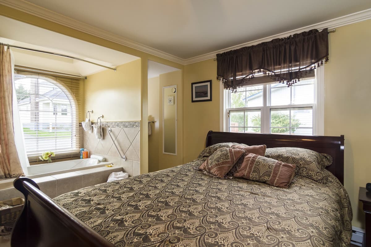 Quarto com uma cama grande, janela com cortinas, banheira e chuveiro.