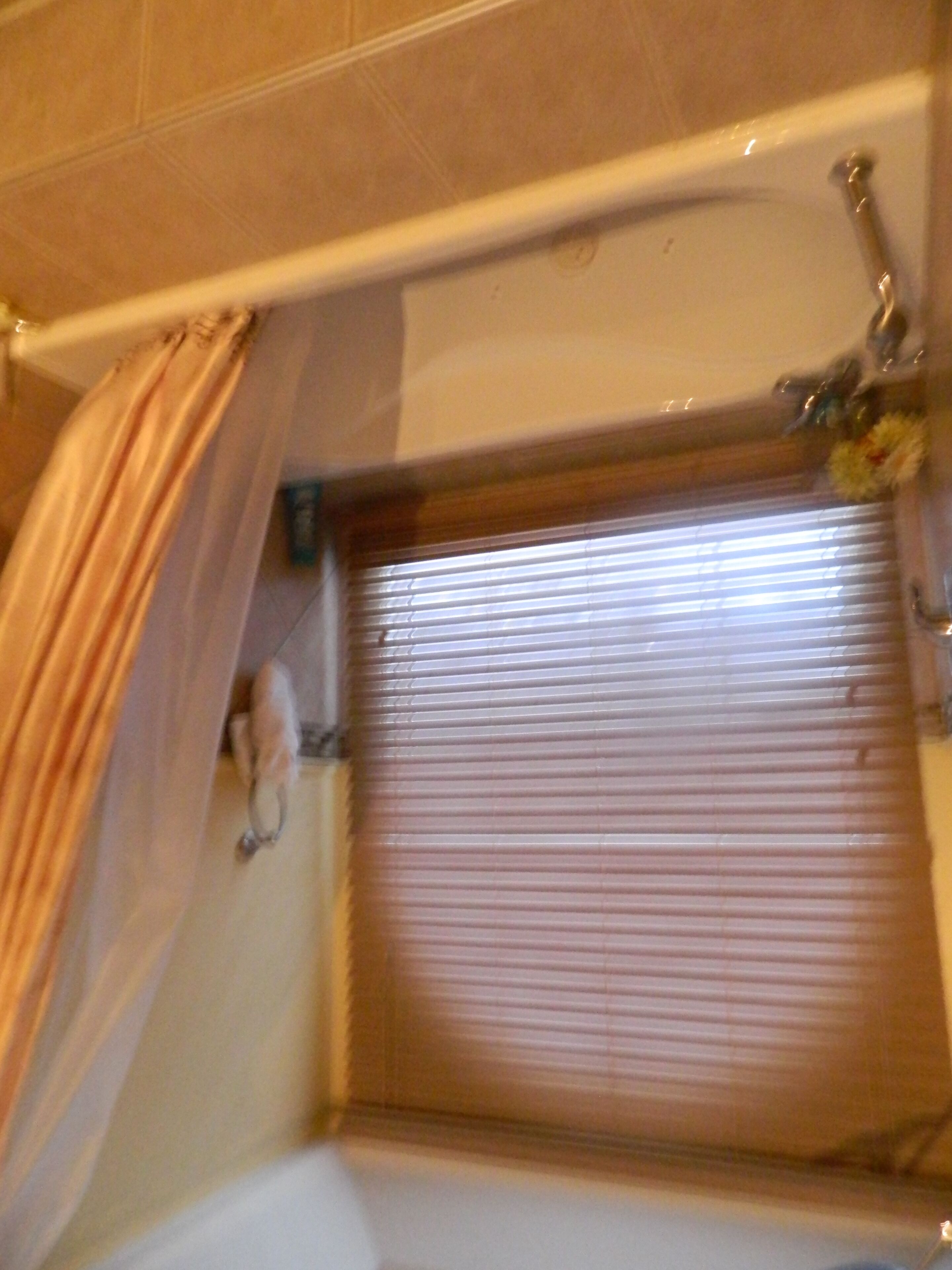 A bathroom with a shower curtain, a bathtub, and a window with blinds.