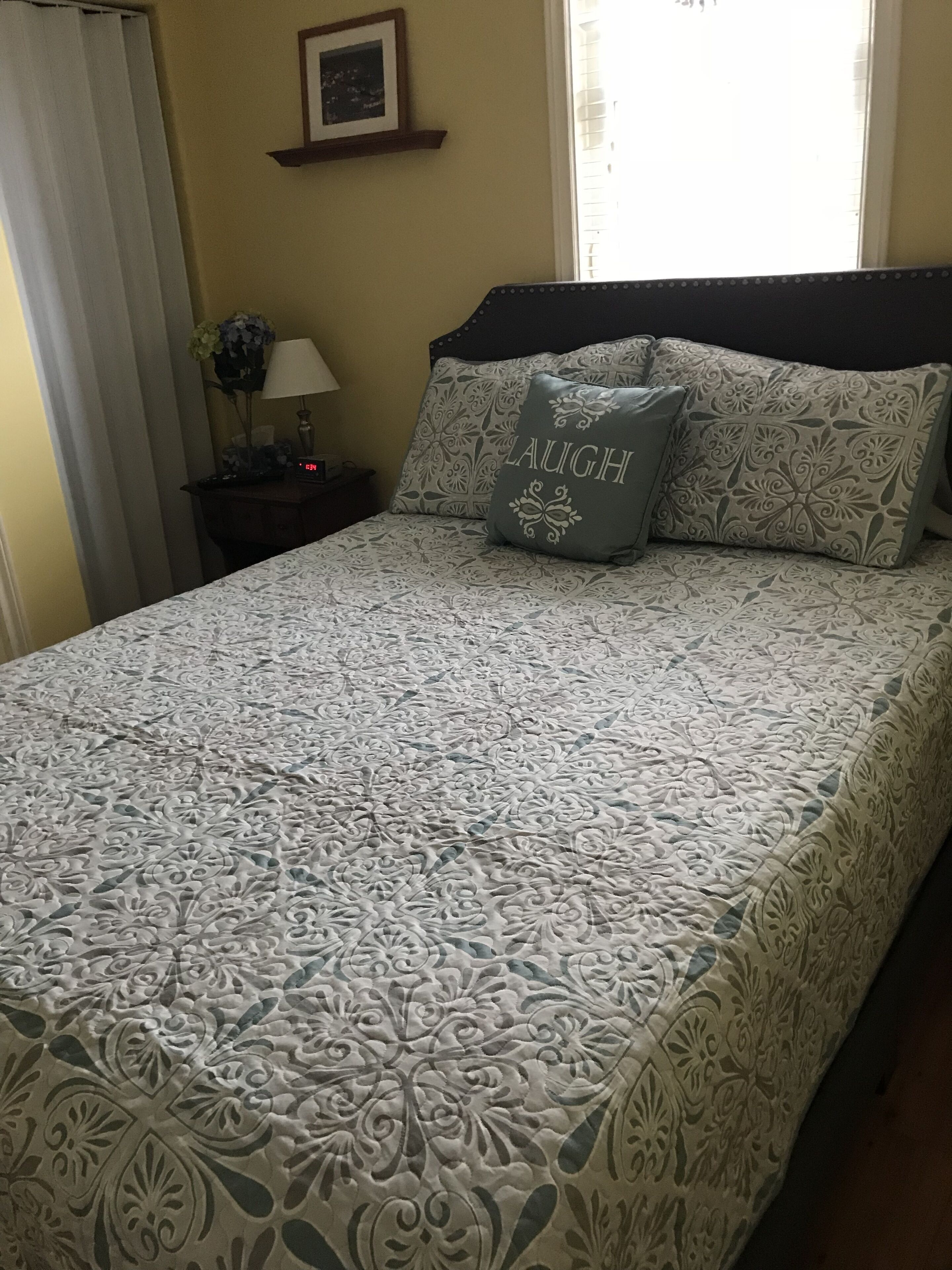 A neatly made bed with a patterned bedspread and two pillows, one with the word "LAUGH" on it.