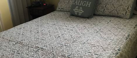 A neatly made bed with a patterned bedspread and two pillows, one with the word "LAUGH" on it.