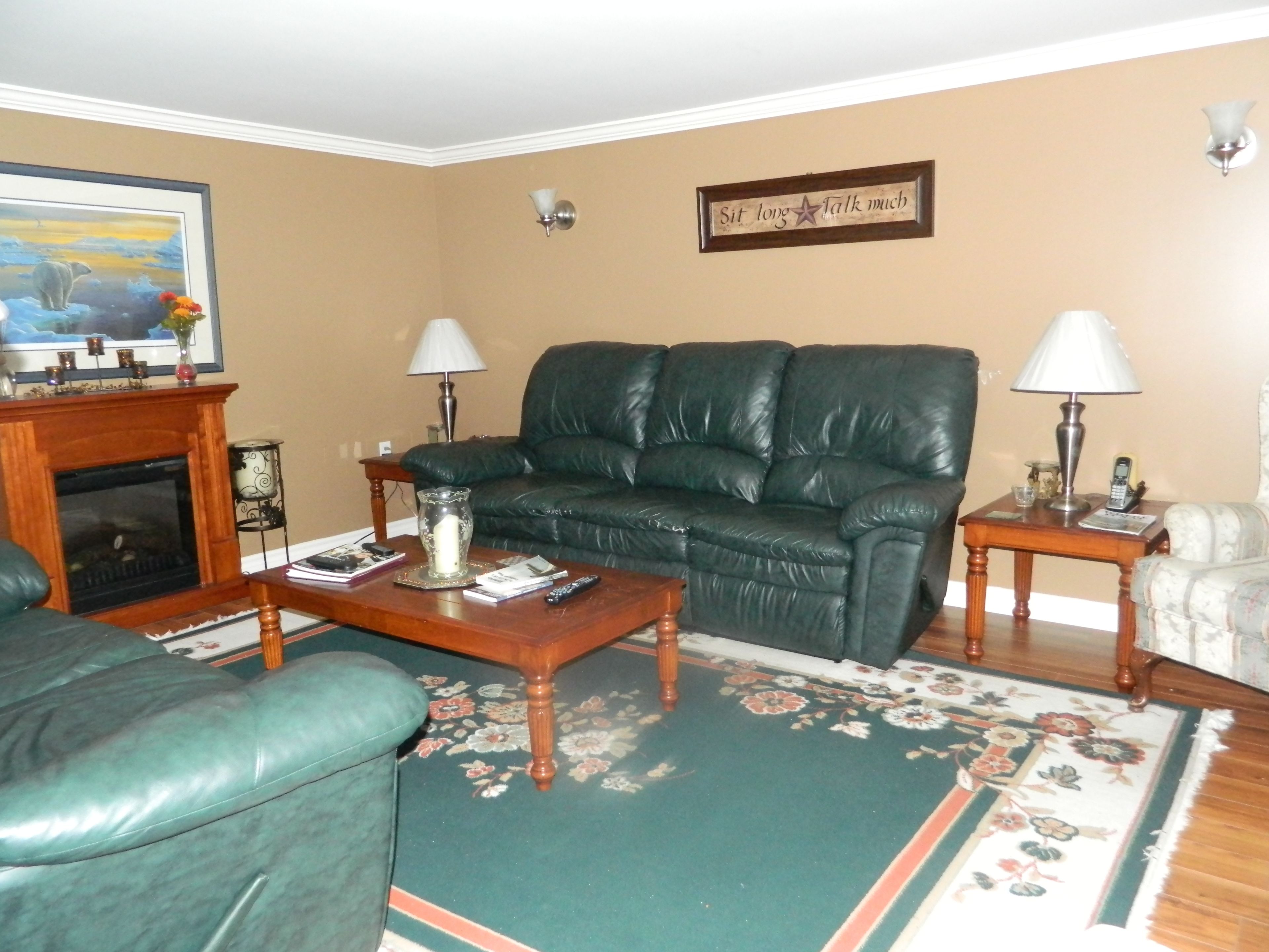 A living room with a green leather sofa, a wooden coffee table, a fireplace, and a floral rug.
